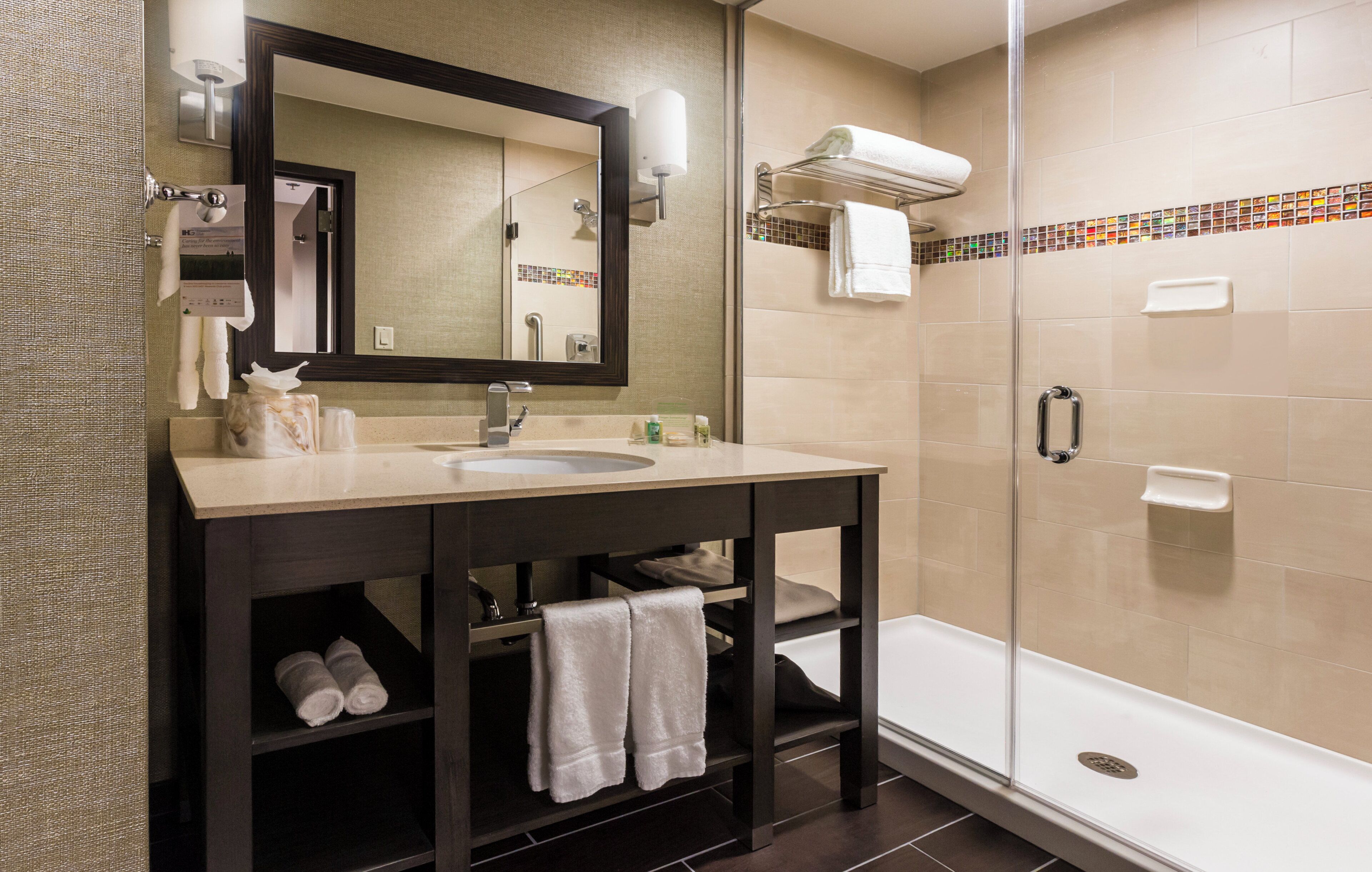 A bathroom with a sink, mirror, towel rack, and a glass-enclosed shower.