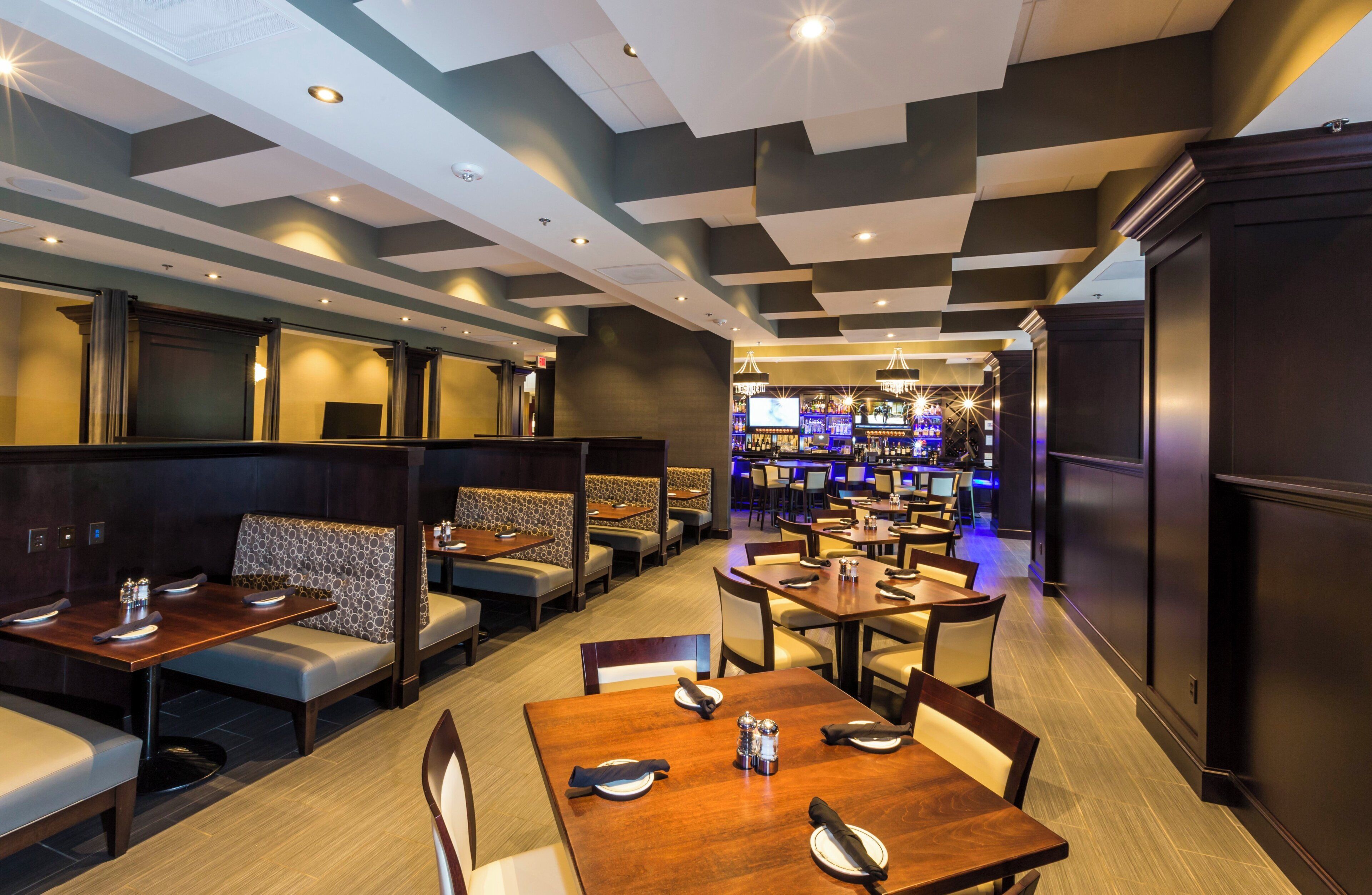 A restaurant with booths and tables, a bar area, and a modern ceiling design.