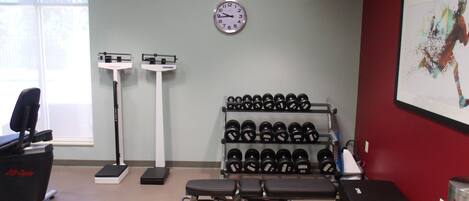 Un gimnasio con equipo de ejercicio, un reloj de pared y una ventana.