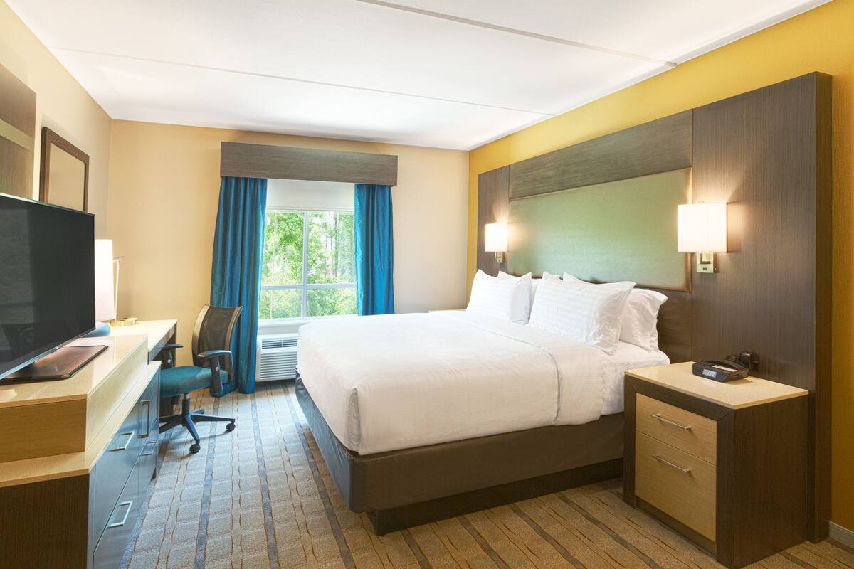 Une chambre d’hôtel comprenant un lit, des tables de chevet, un bureau avec une chaise, une télévision et une fenêtre avec des rideaux.