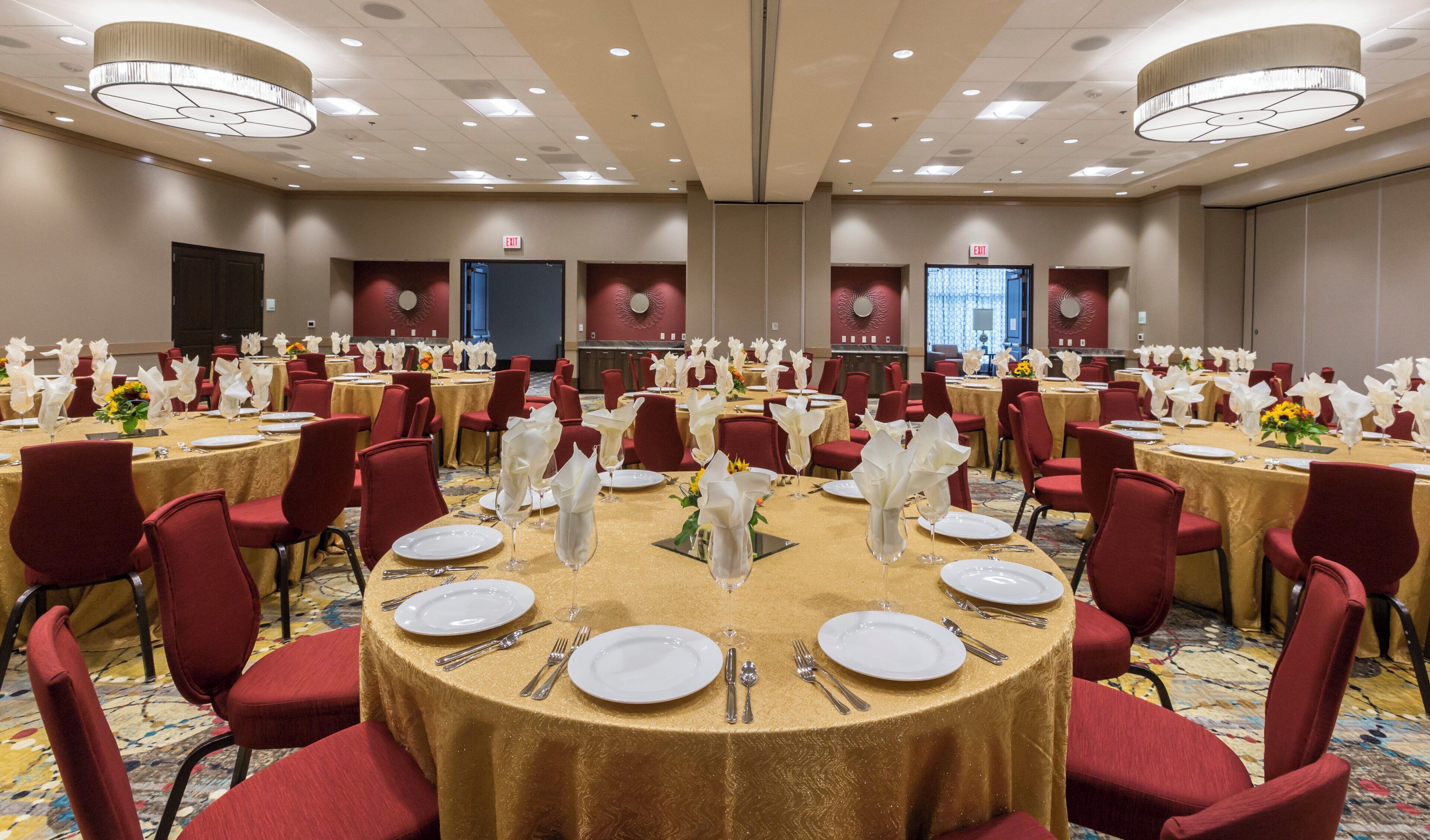 A banquet hall with round tables, red chairs, and gold tablecloths.
