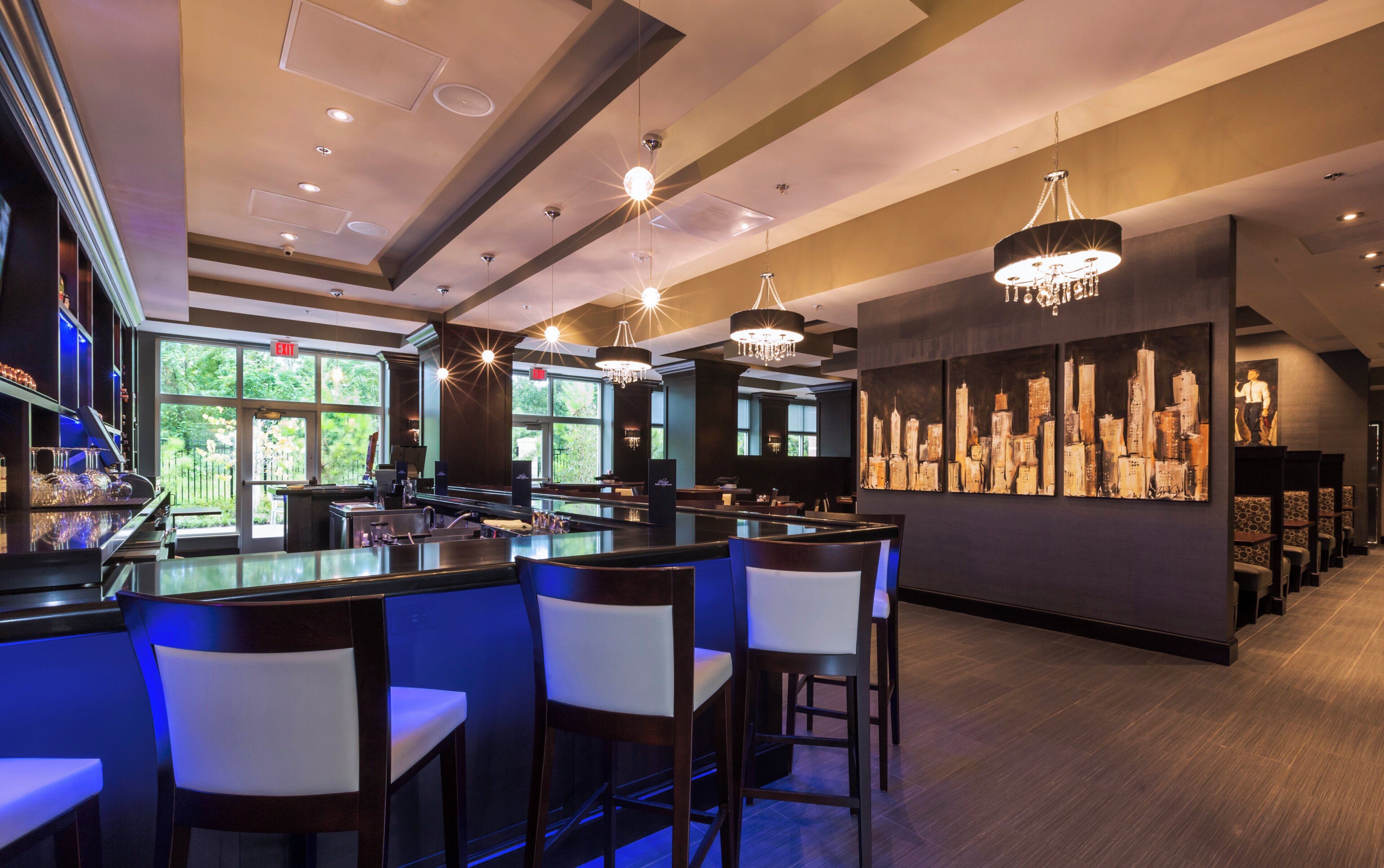 A bar area with multiple seating options, a cityscape mural, and a view of greenery outside.