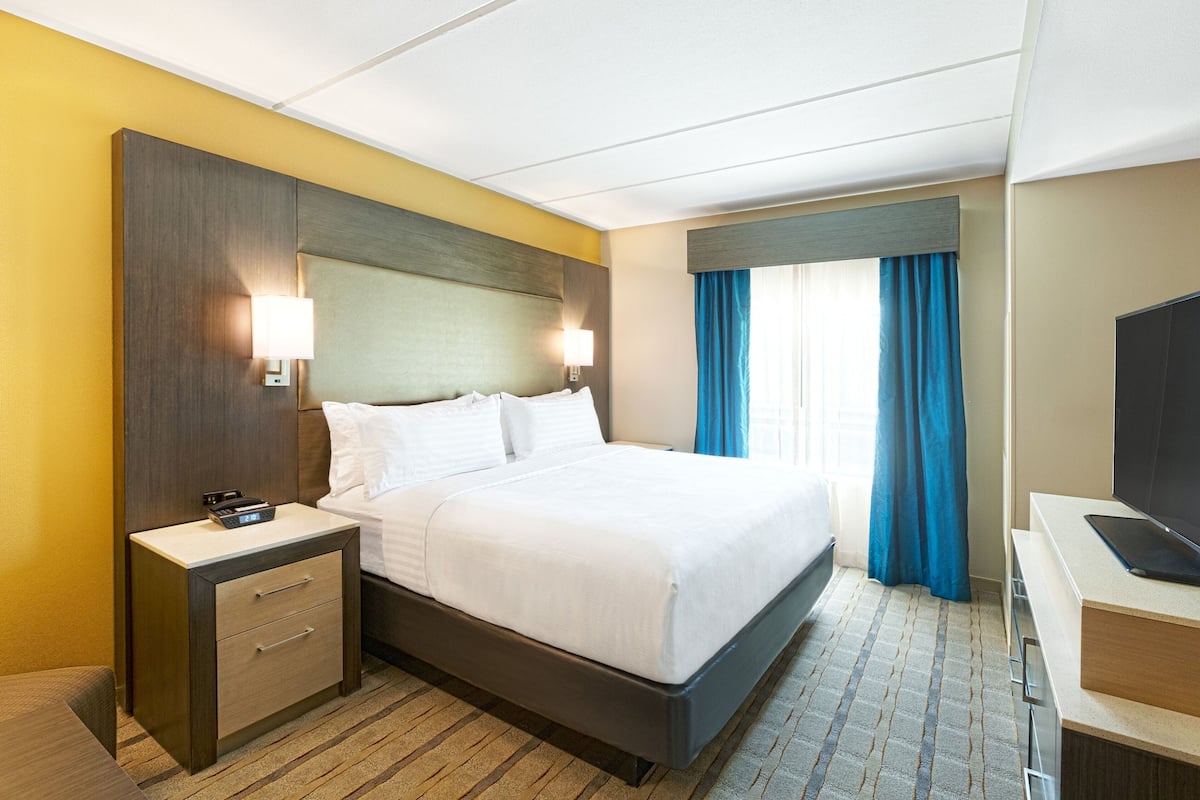Une chambre d’hôtel comprenant un lit, des tables de chevet, un bureau avec un téléviseur à écran plat et une fenêtre avec des rideaux.