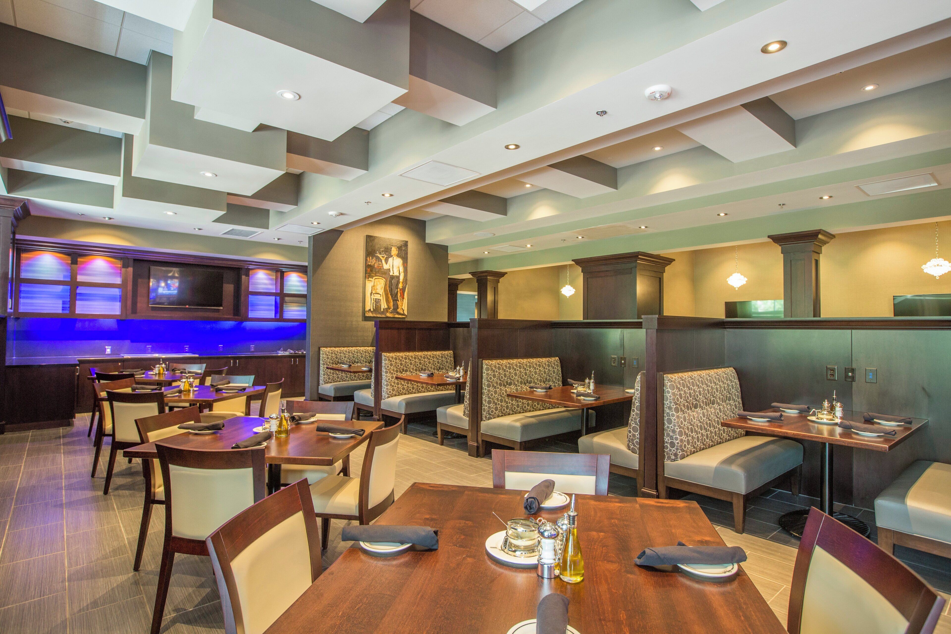 A restaurant with booths and tables, a bar area with a TV, and a ceiling with recessed lighting.