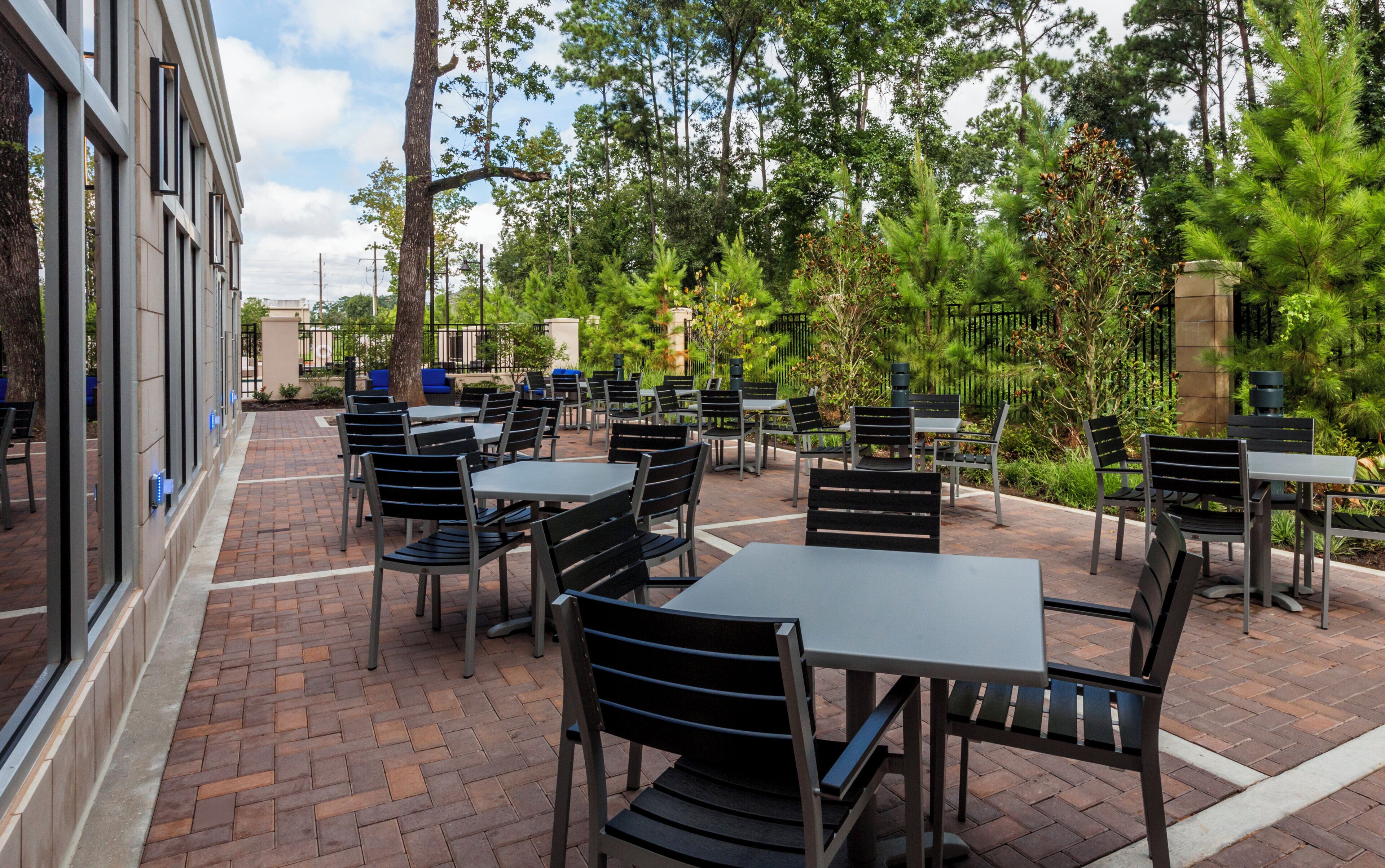 An outdoor patio with tables and chairs, surrounded by greenery and trees.
