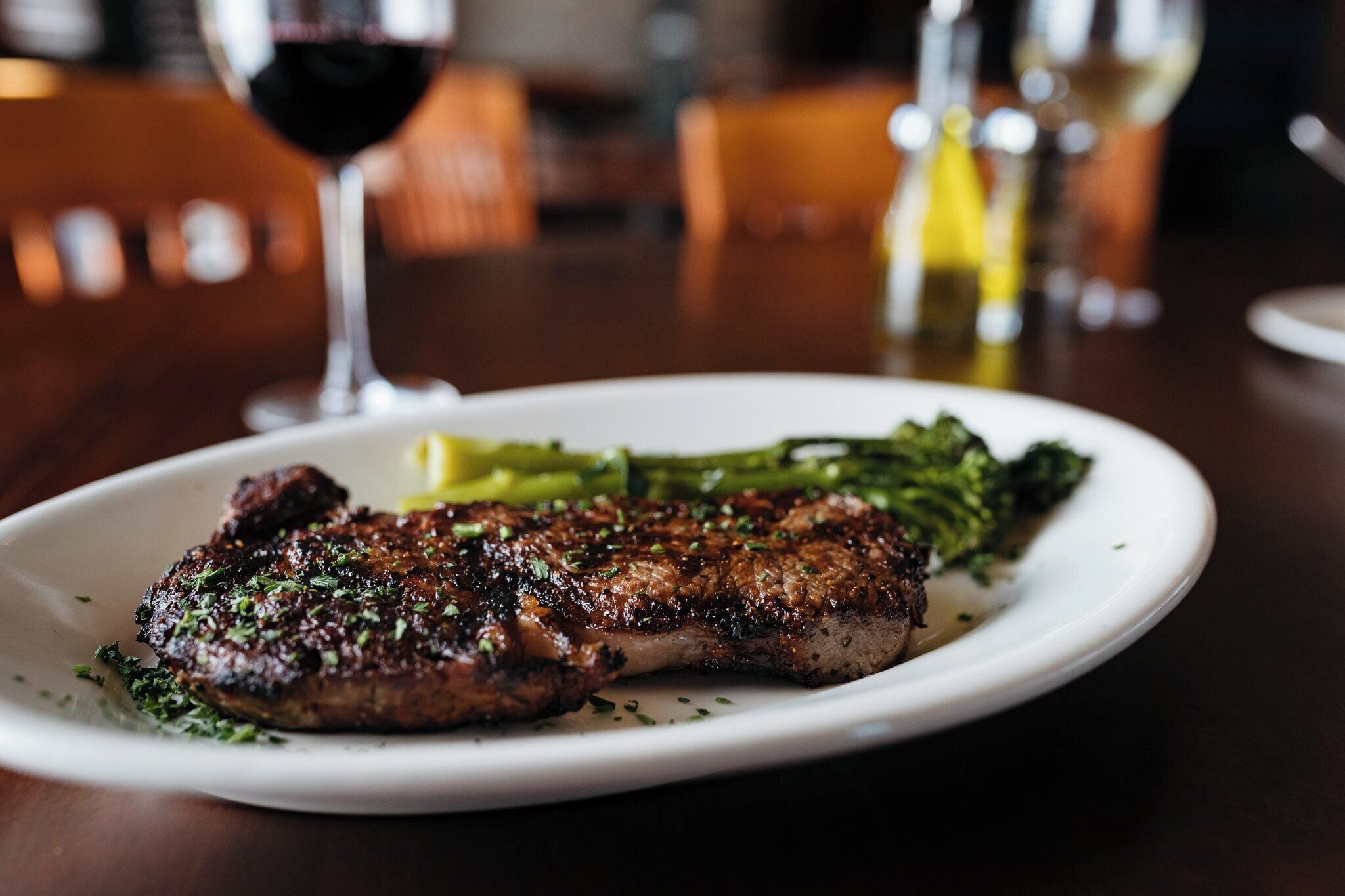 A plate of grilled steak with a side of broccoli and lemon wedges on a white plate.
