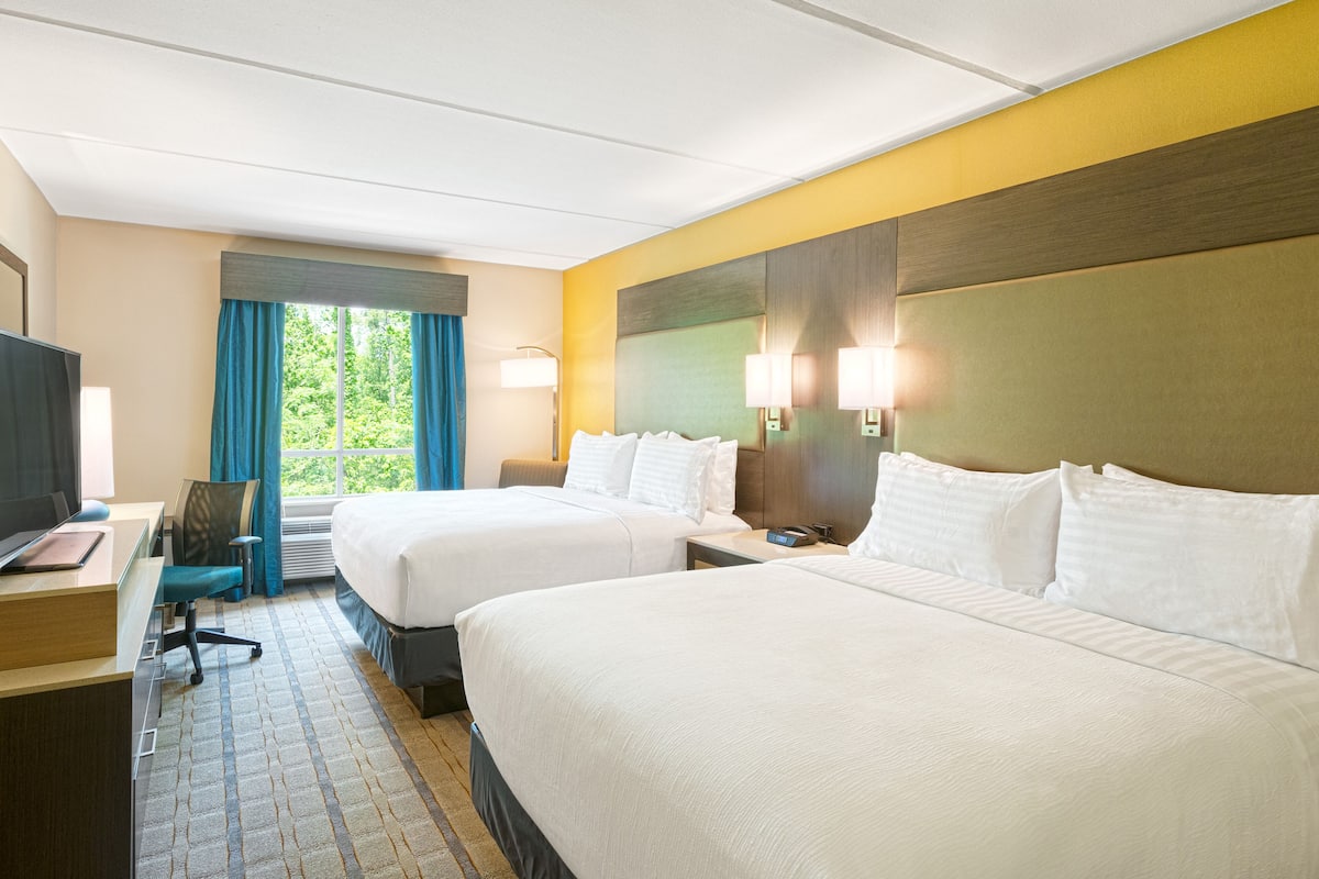 Une chambre d’hôtel avec deux lits, un bureau avec un ordinateur, une chaise et une fenêtre avec des rideaux.