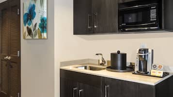 A modern kitchen with dark wood cabinets, a stainless steel sink, a microwave, and a coffee maker.