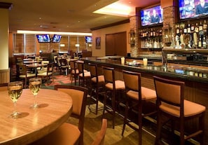 A bar area with multiple seating options, including round tables and bar stools, and a well-stocked bar with various bottles. - Crowne Plaza Shenandoah - Woodlands Area by IHG (Shenandoah)