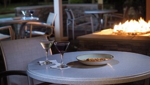 An outdoor dining area with a round table, two empty martini glasses, a bowl of food, and a fire feature in the background. - SpringHill Suites by Marriott Houston Hwy. 290/NW Cypress (Houston)