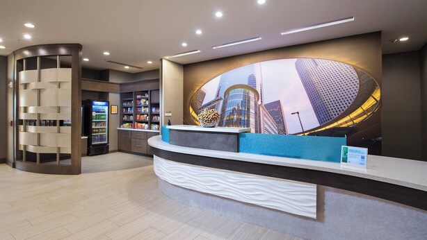 A modern reception area with a curved counter, a vending machine, and a large digital display of a cityscape. - SpringHill Suites by Marriott Houston Hwy. 290/NW Cypress (Houston)