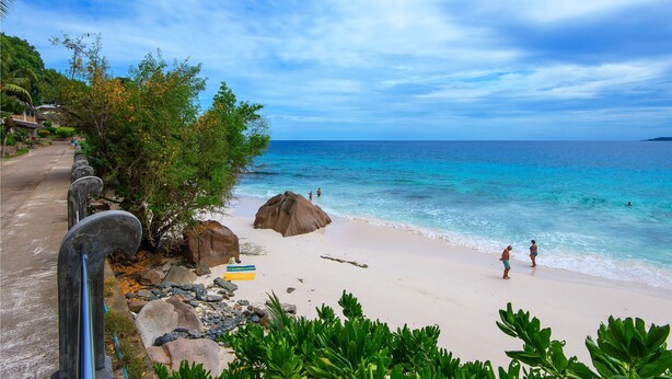 Uma praia com águas azul-claras, areal arenoso e algumas pessoas caminhando.