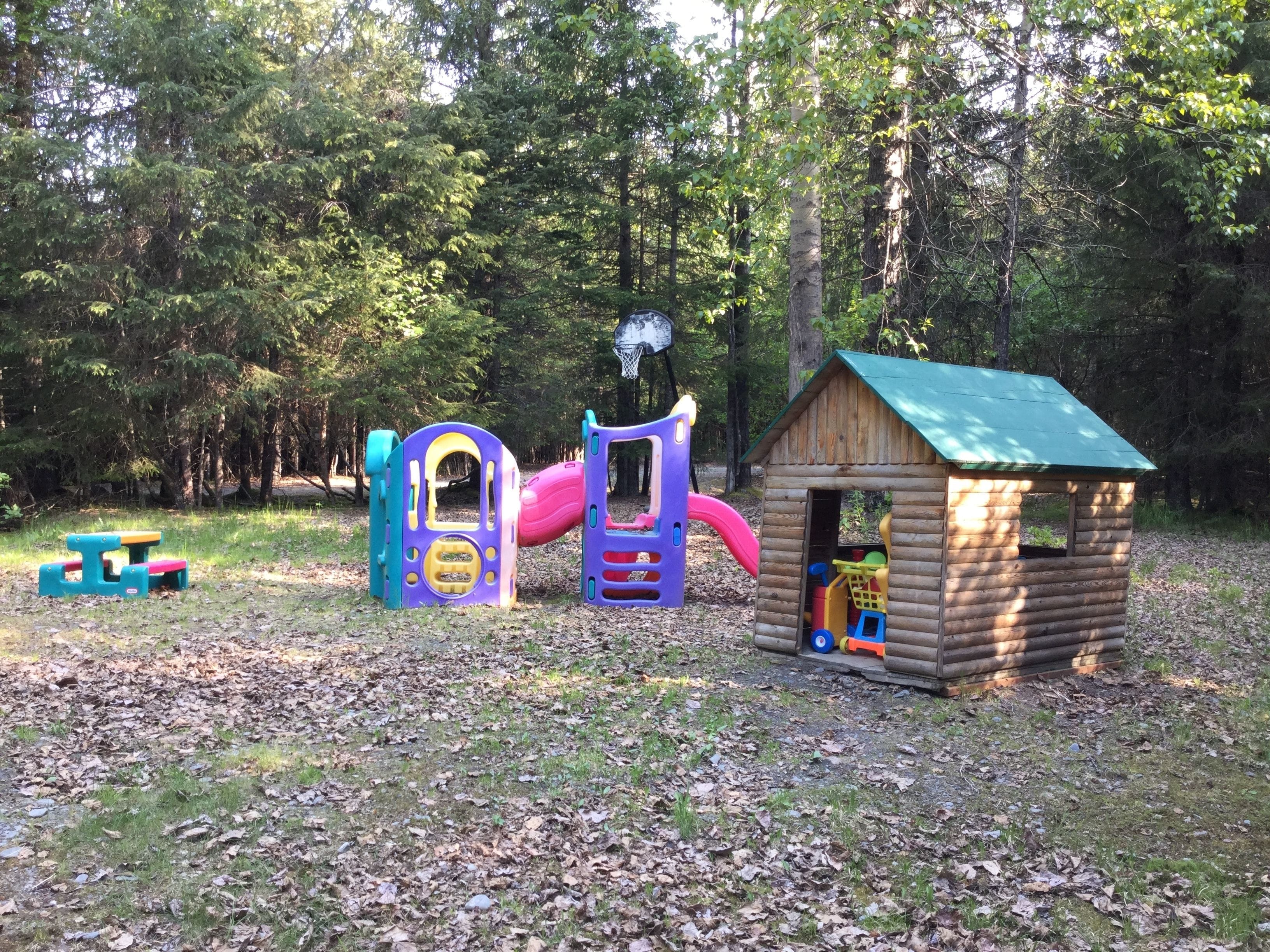 Un parque infantil con tobogán, estructuras para escalar y una pequeña casita de madera.