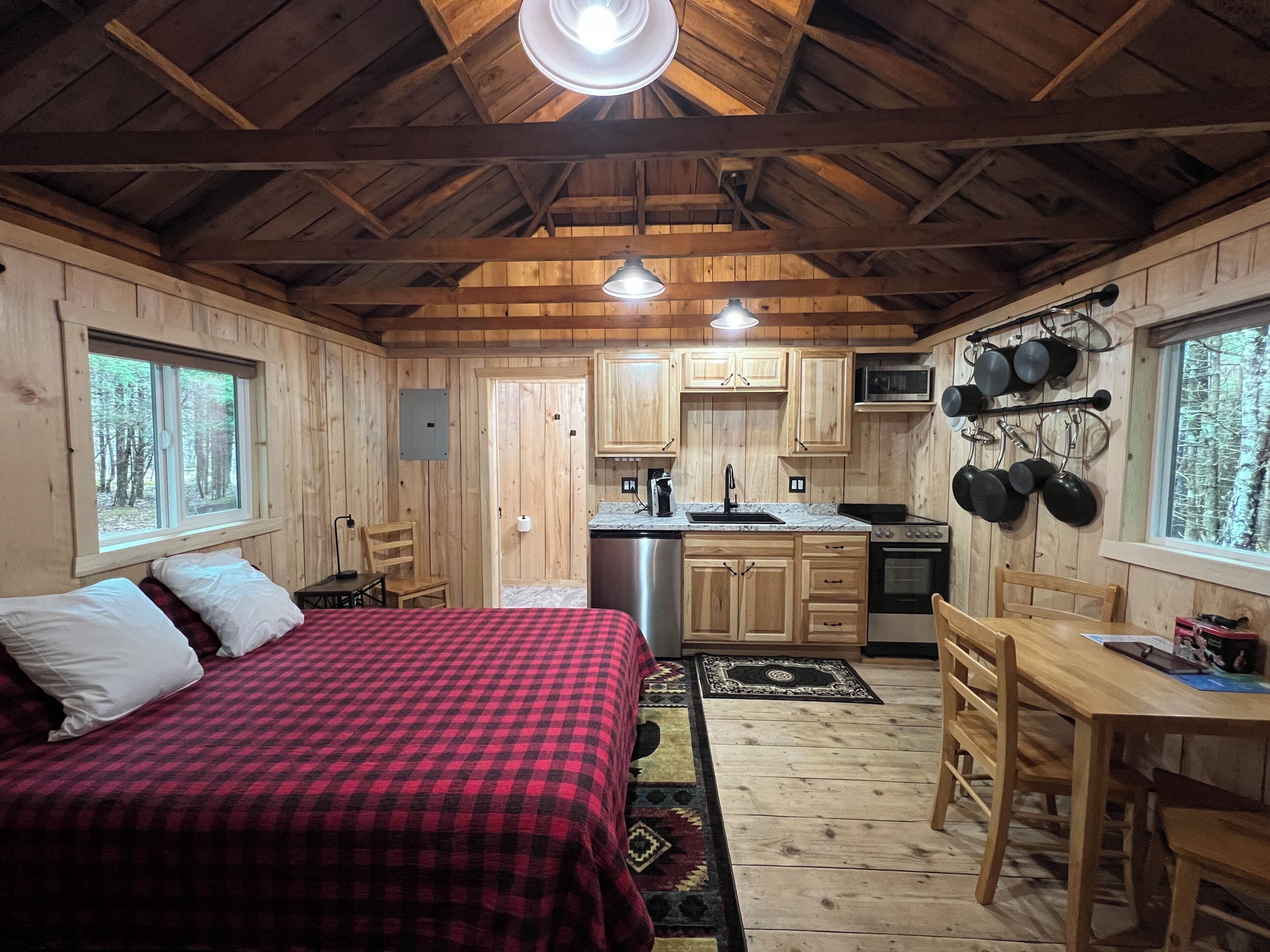 A cabin interior with a bed, wooden walls, a kitchen area, and a dining table.