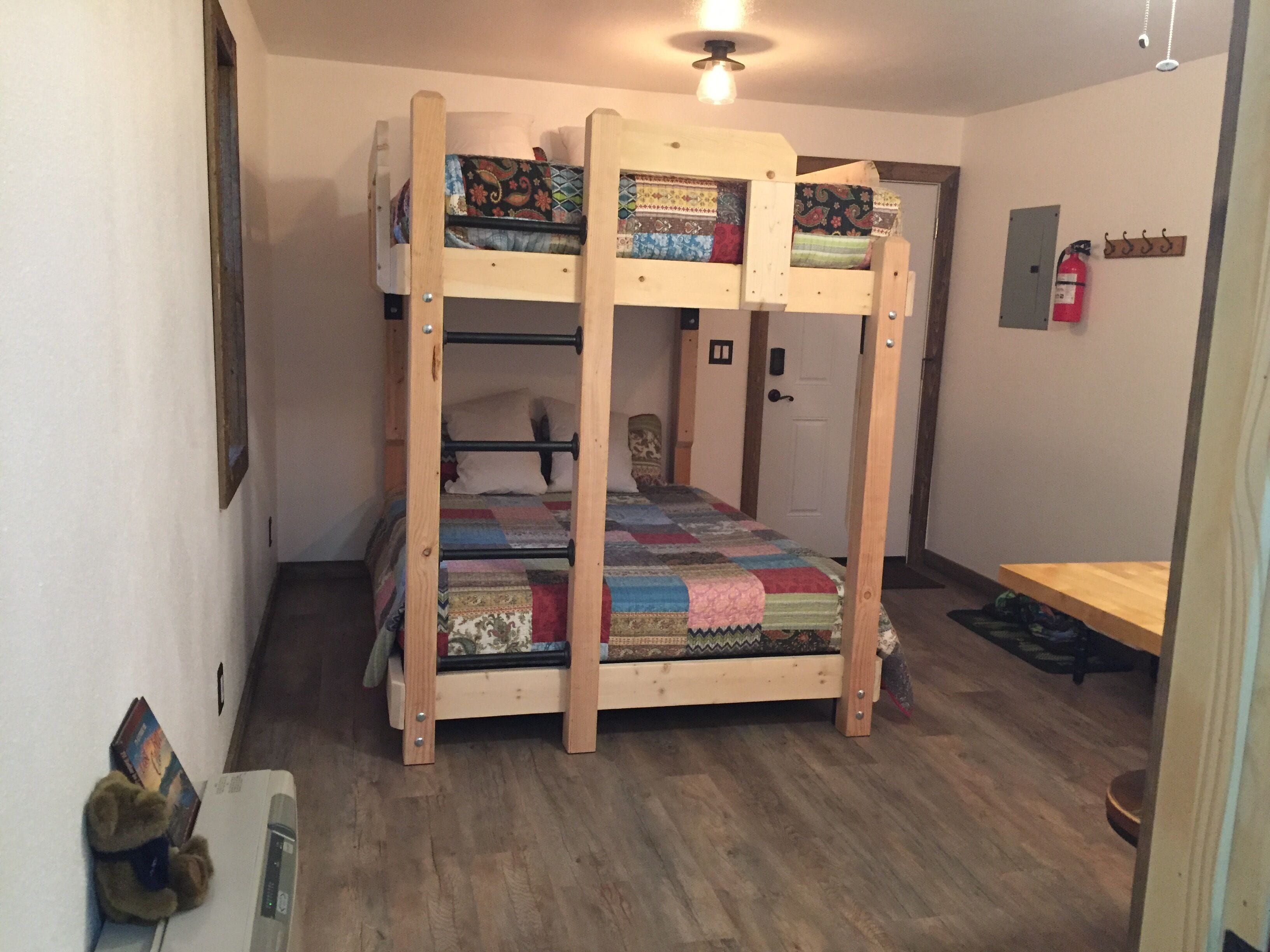 Ein Stockbett mit Decke, ein Holztisch und ein Feuerlöscher an der Wand.