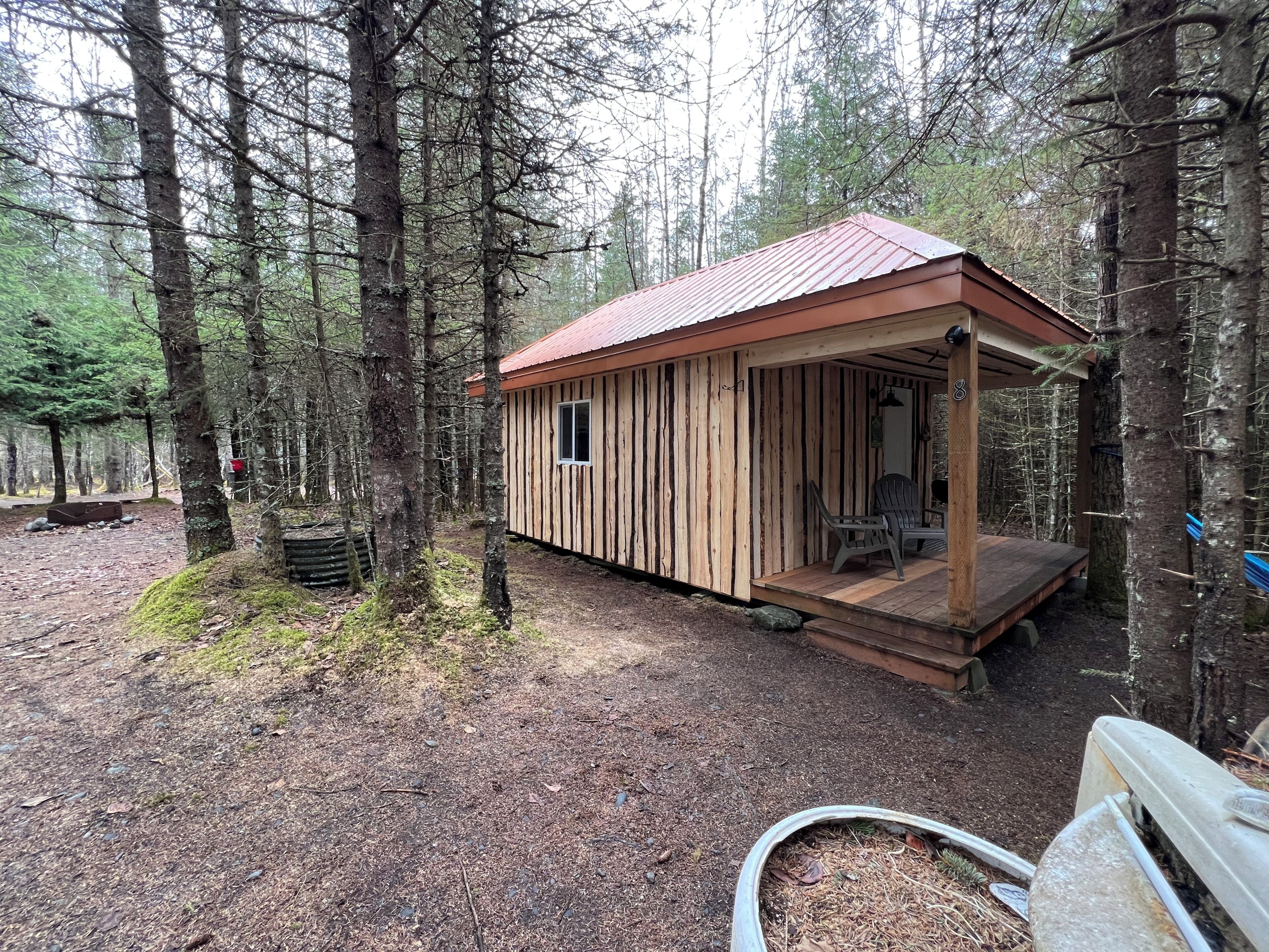 Une cabane en bois avec un porche, entourée d’arbres.