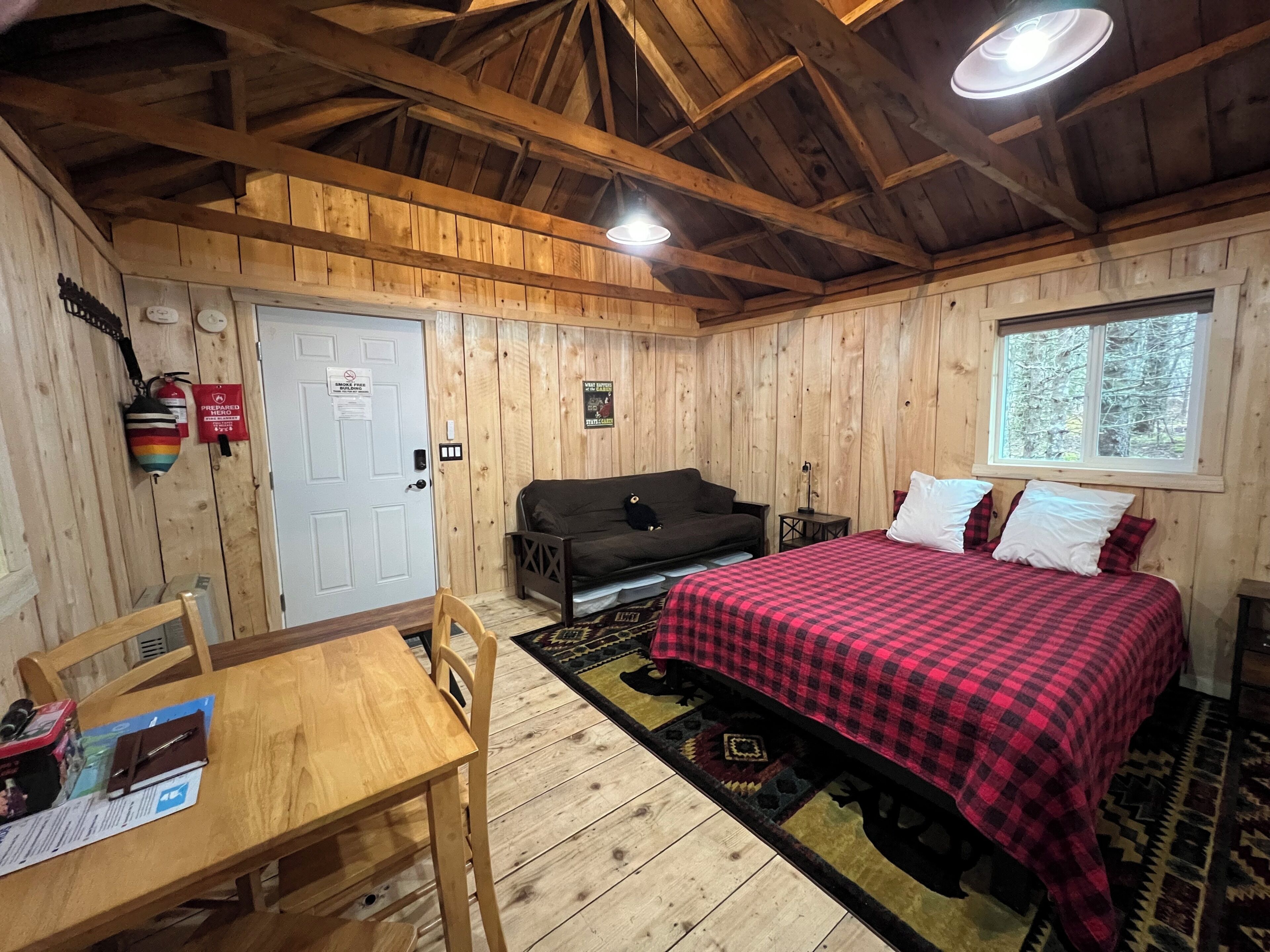 L’intérieur d’un chalet en bois, avec un lit, un canapé, une table et une fenêtre.