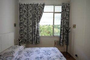 A bedroom with a bed, a window with curtains, a radiator, and a coat rack. - Ribeiro 612 (Rio de Janeiro)