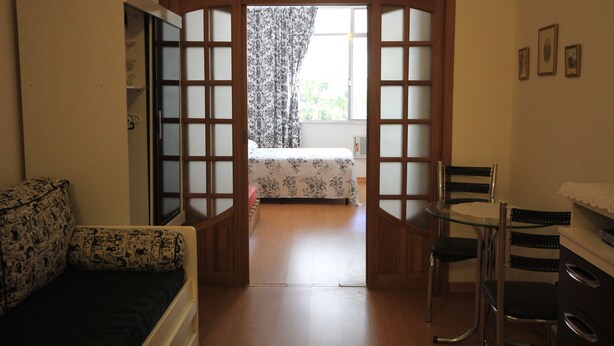A room with a bed, a small table, and a chair. There is a window with curtains, and a door leading to another room. - Ribeiro 612 (Rio de Janeiro)