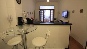 A compact kitchen with a glass table, a white chair, a ceiling fan, a television, and a view into the living area. - Ribeiro 612 (Rio de Janeiro)