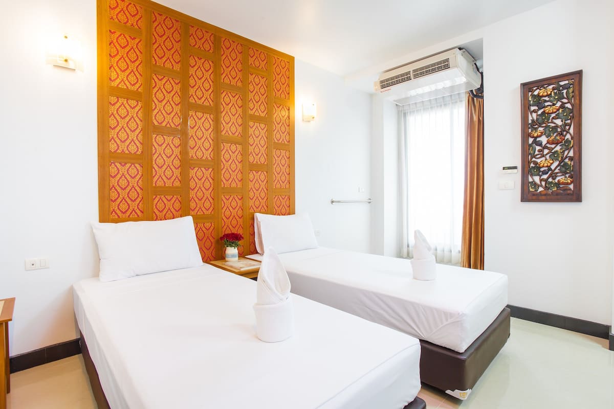 Une chambre d’hôtel avec deux lits simples, un panneau décoratif au mur, un appareil de climatisation et une fenêtre avec des rideaux.