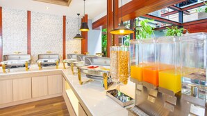 Uma área de buffet com várias estações de serviço, incluindo um bar de sucos e um bar de saladas.