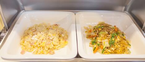 Two white rectangular dishes of fried rice, one with visible ham and the other with vegetables, in a stainless steel buffet setting.