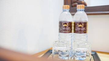 Two bottles of New Siam drinking water and three glasses on a tray.