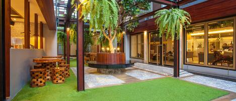 A modern outdoor area with artificial grass, wooden tables, and hanging plants.