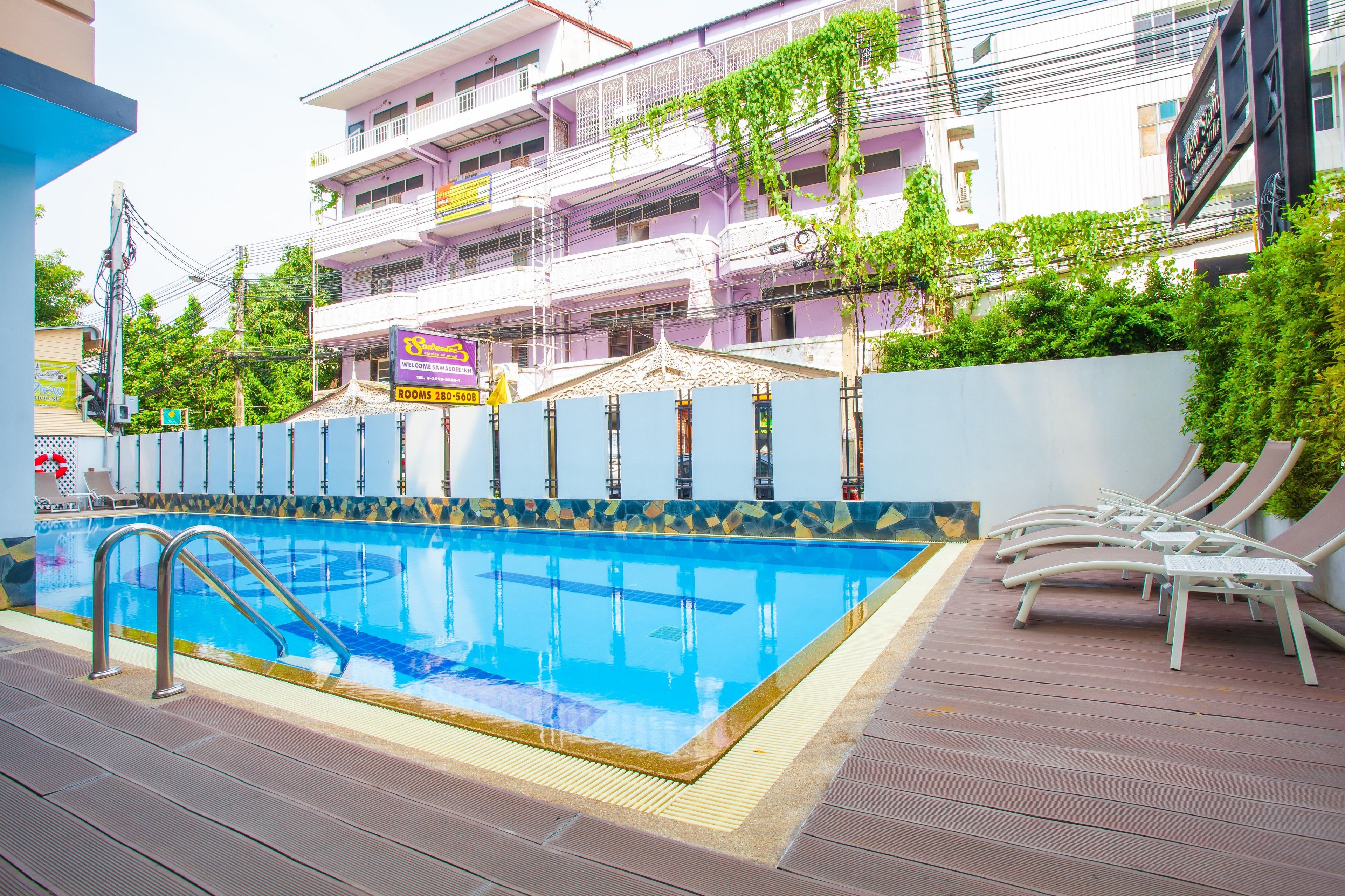 A swimming pool with a tiled deck, lounge chairs, and a building with balconies in the background.