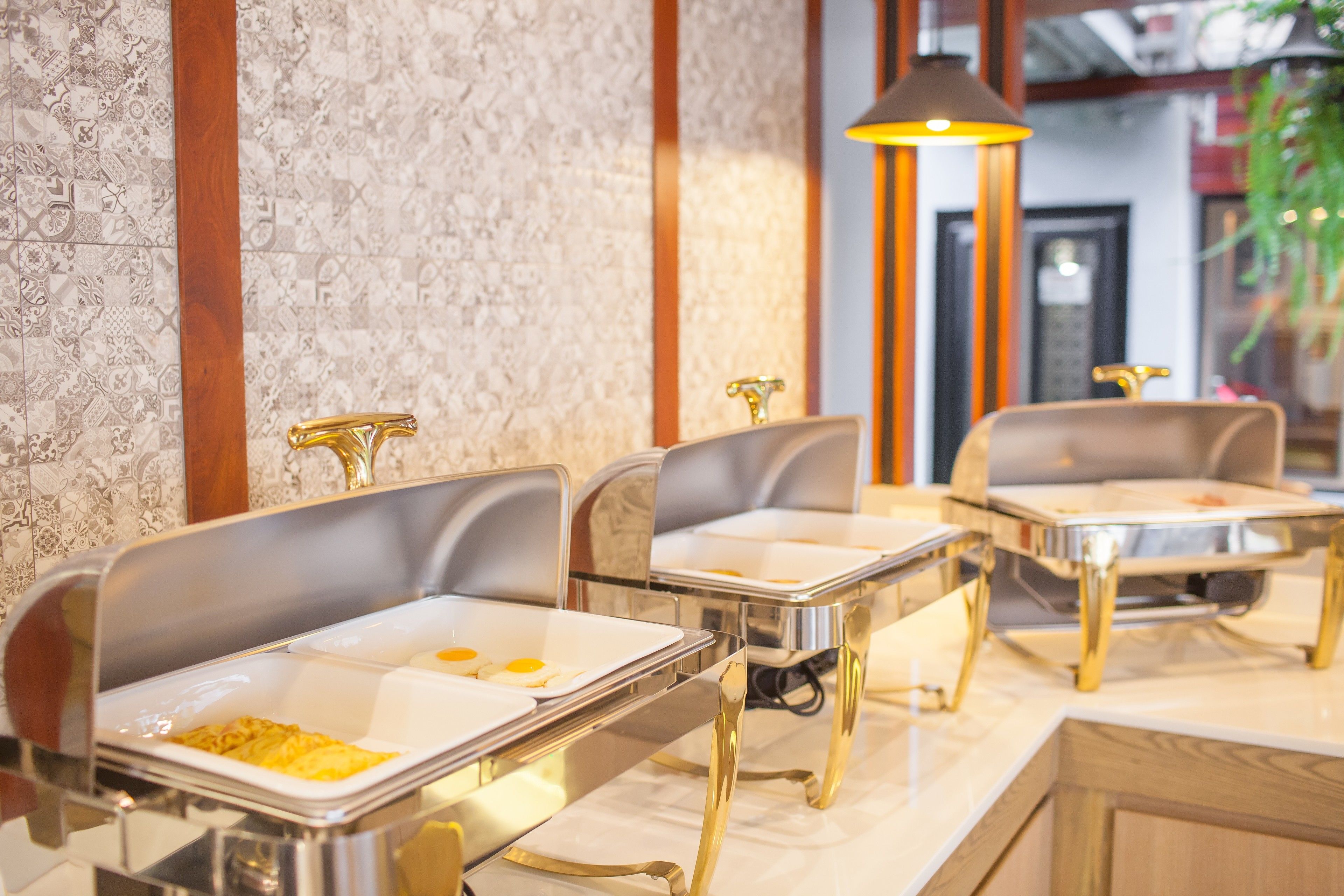 A buffet setup with modern, metallic serving trays and chairs, set against a textured wall with a patterned design.