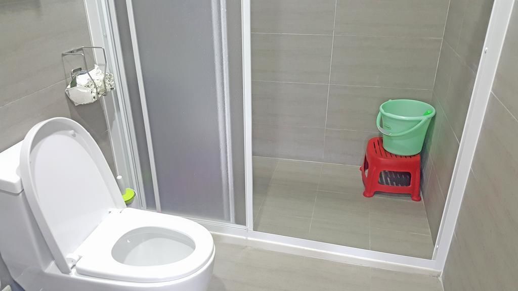 Un baño con inodoro, cabina de ducha y un cubo verde sobre un taburete rojo.