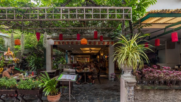 An outdoor cafe area with tables and chairs, surrounded by potted plants and a wooden pergola. - New Siam I (Bangkok)