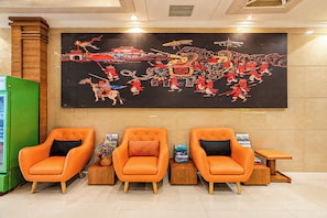 A reception area with three orange chairs, a large traditional artwork on the wall, and a green refrigerator. - Two Elephants Hotel (Ho Chi Minh City)