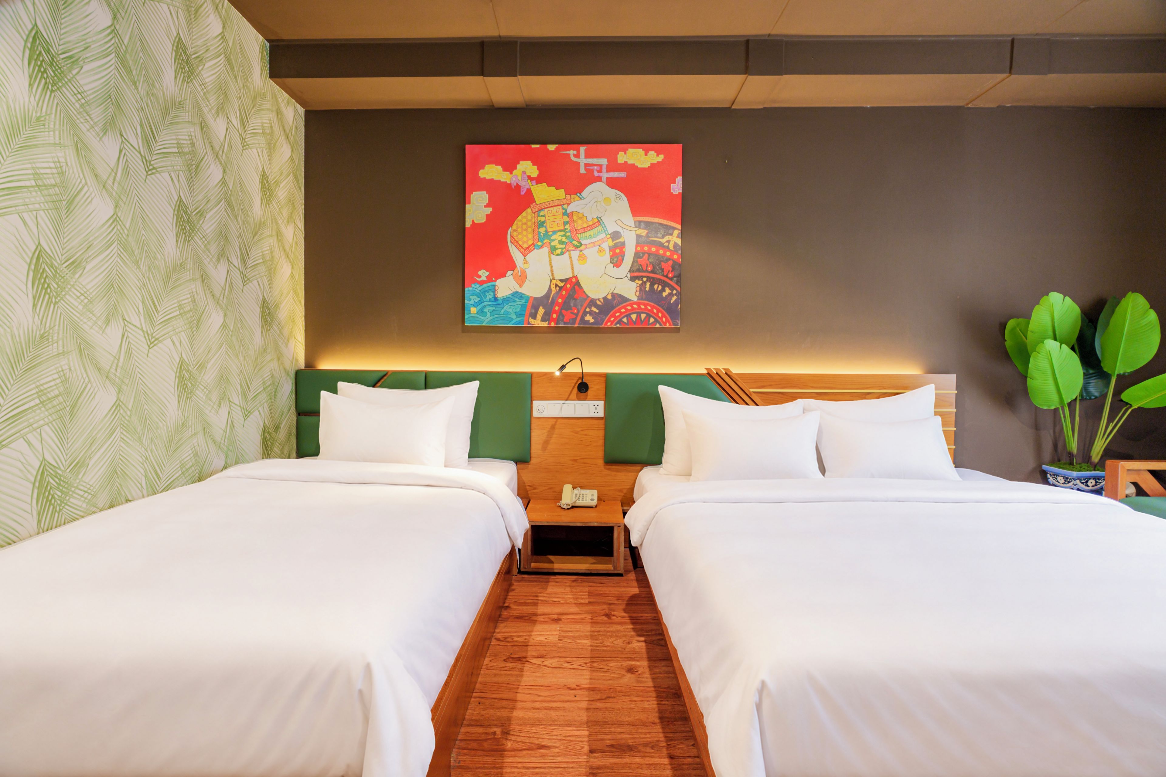 A hotel room with two beds, a green headboard, a painting on the wall, and a wooden floor.