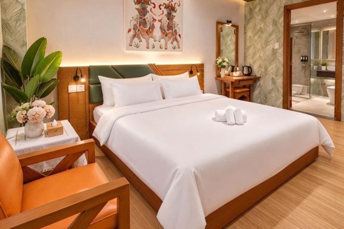 Habitación de hotel con una cama grande, una mesita de noche con lámpara, una silla y vista al baño.