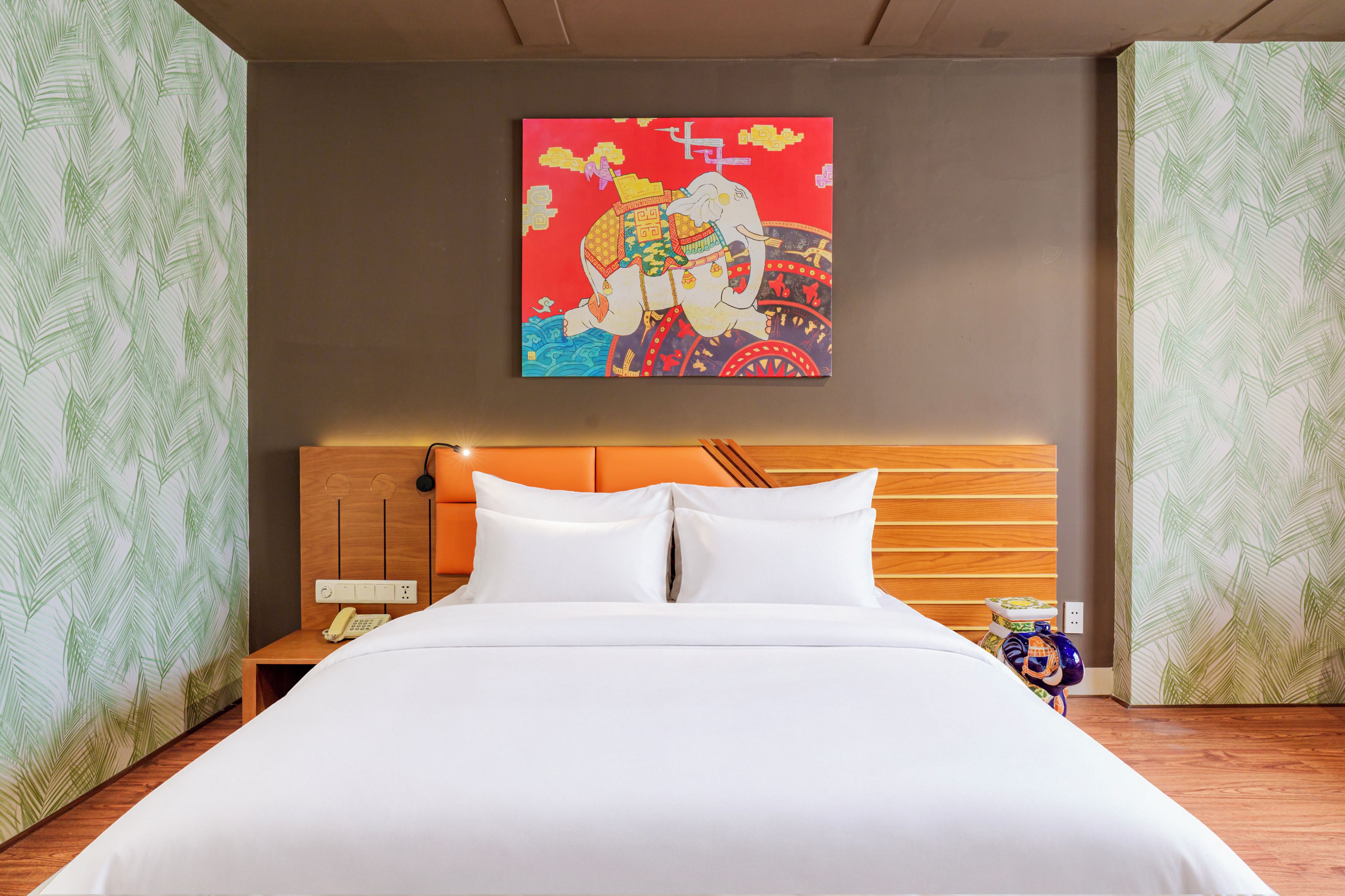 Ein Hotelzimmer mit Bett, Nachttisch, Telefon und einer Wand mit einem farbenfrohen Gemälde.
