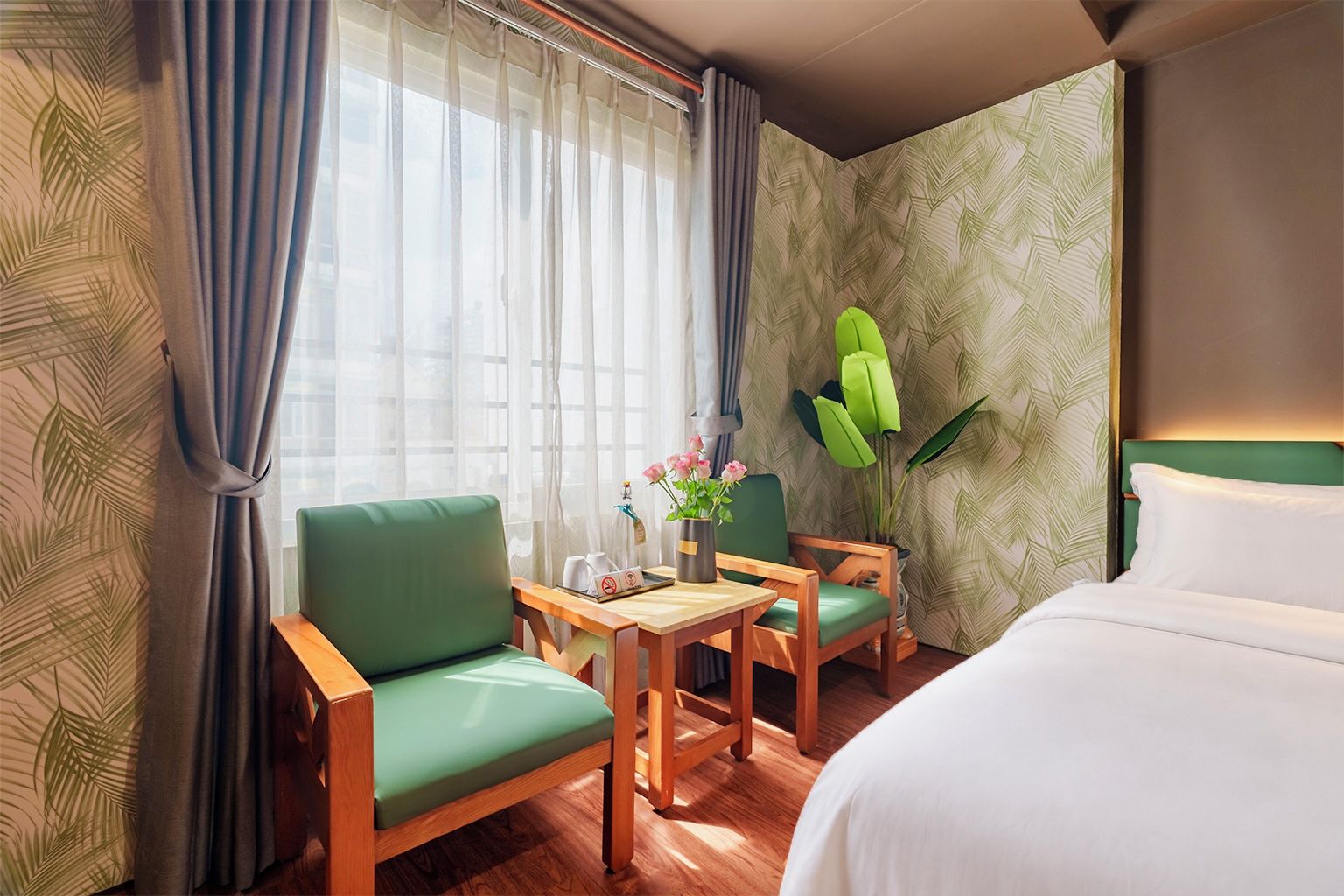 A hotel room with a bed, two chairs, a small table, and a potted plant.