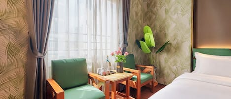 Une chambre d’hôtel avec un lit, deux chaises, une petite table et une plante en pot.