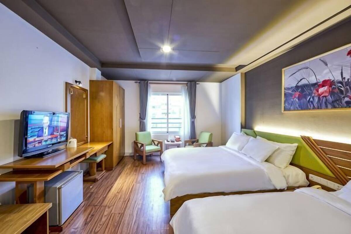 Habitación de hotel con dos camas, un escritorio con televisor, un pequeño rincón de descanso y un cuadro en la pared.
