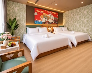 Habitación de hotel con dos camas, una mesa de comedor con fruta y un cuadro grande en la pared.