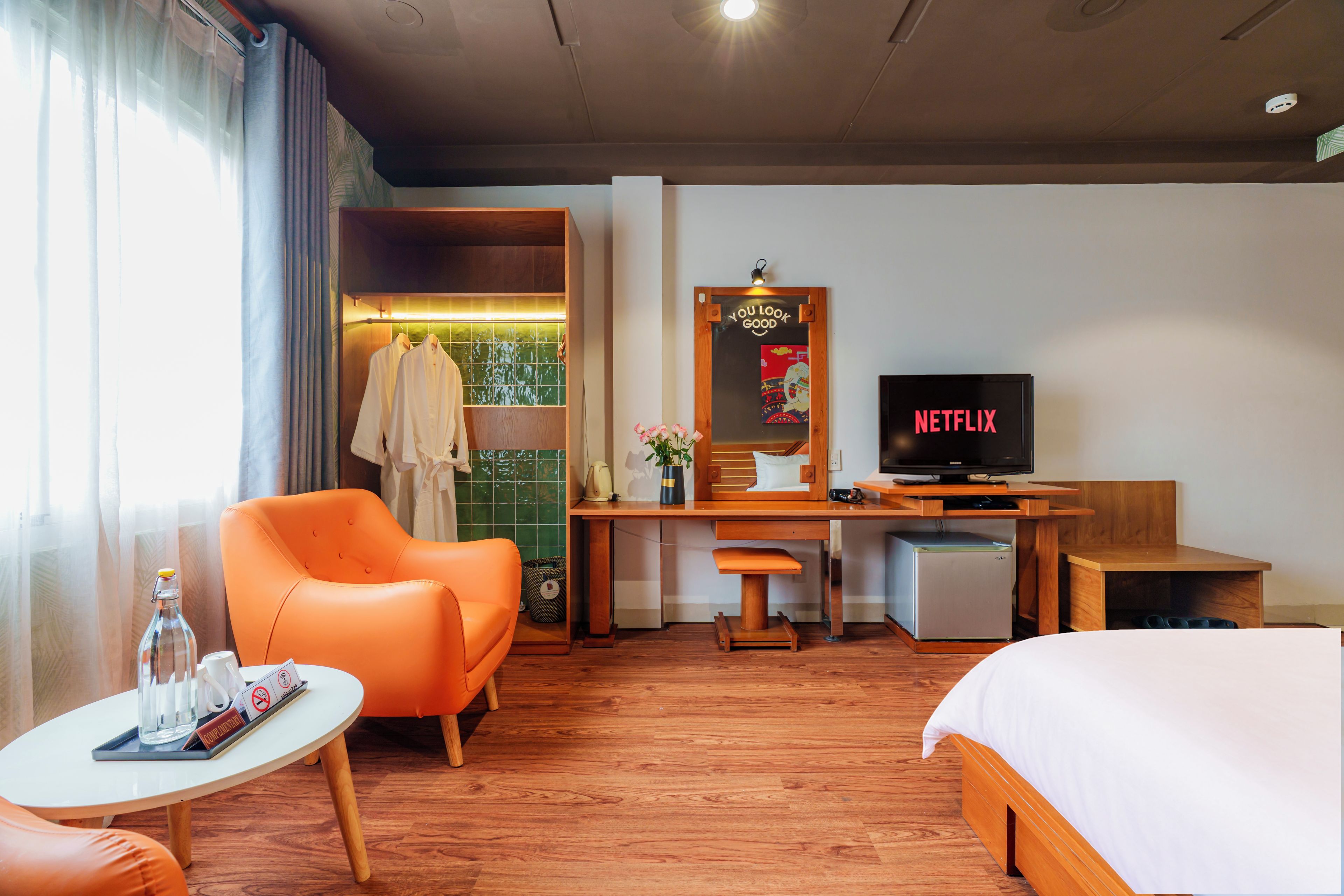 Habitación de hotel con cama, escritorio con televisor, silla, mesita y ventana con cortinas.