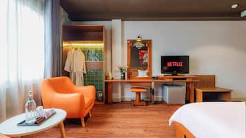 A hotel room with a bed, a desk with a television, a chair, a small table, and a window with curtains.