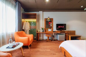 Habitació d'hotel amb un llit, un escriptori amb televisió, una cadira, una taula petita i una finestra amb cortines.