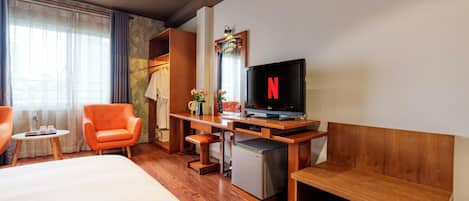 A hotel room with a bed, a desk with a television, a chair, and a small refrigerator.