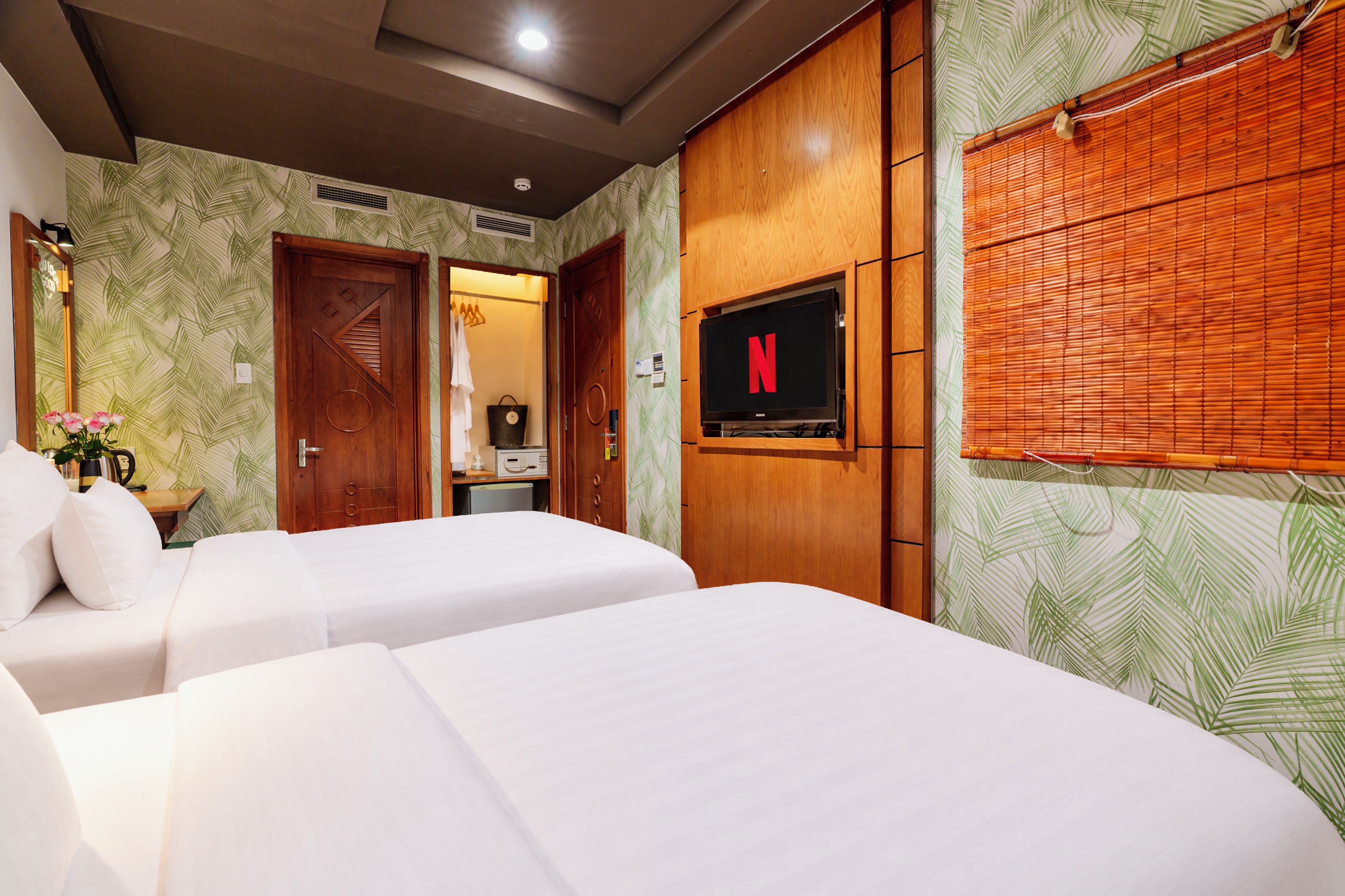 Une chambre d’hôtel avec deux lits, un téléviseur fixé au mur et une armoire en bois.