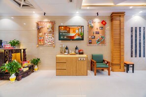 Een receptie met een houten balie, een televisiescherm waarop 'Sauna & Jacuzzi' staat, en een muur met diverse decoraties.