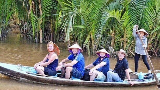 A group of people in a traditional boat on a river surrounded by dense vegetation. - Two Elephants Hotel (Ho Chi Minh City)
