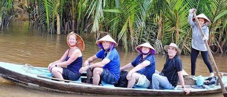 Un groupe de personnes se trouve dans un bateau traditionnel sur une rivière, entourée d’une végétation luxuriante.
