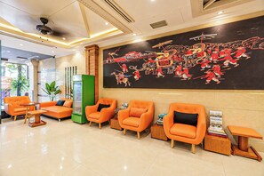 Un hall d’hôtel avec des sièges orange, une grande fresque murale et un comptoir d’accueil.